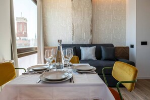 Un coin repas avec une table dressée pour quatre personnes, une bouteille d’eau et une vue sur un bâtiment par la fenêtre.