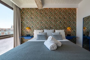 A hotel room with a bed, pillows, a rolled towel, two nightstands with lamps, and a large window. - Sol Atelier | Apartments by Monaro* * * * * (Madrid)