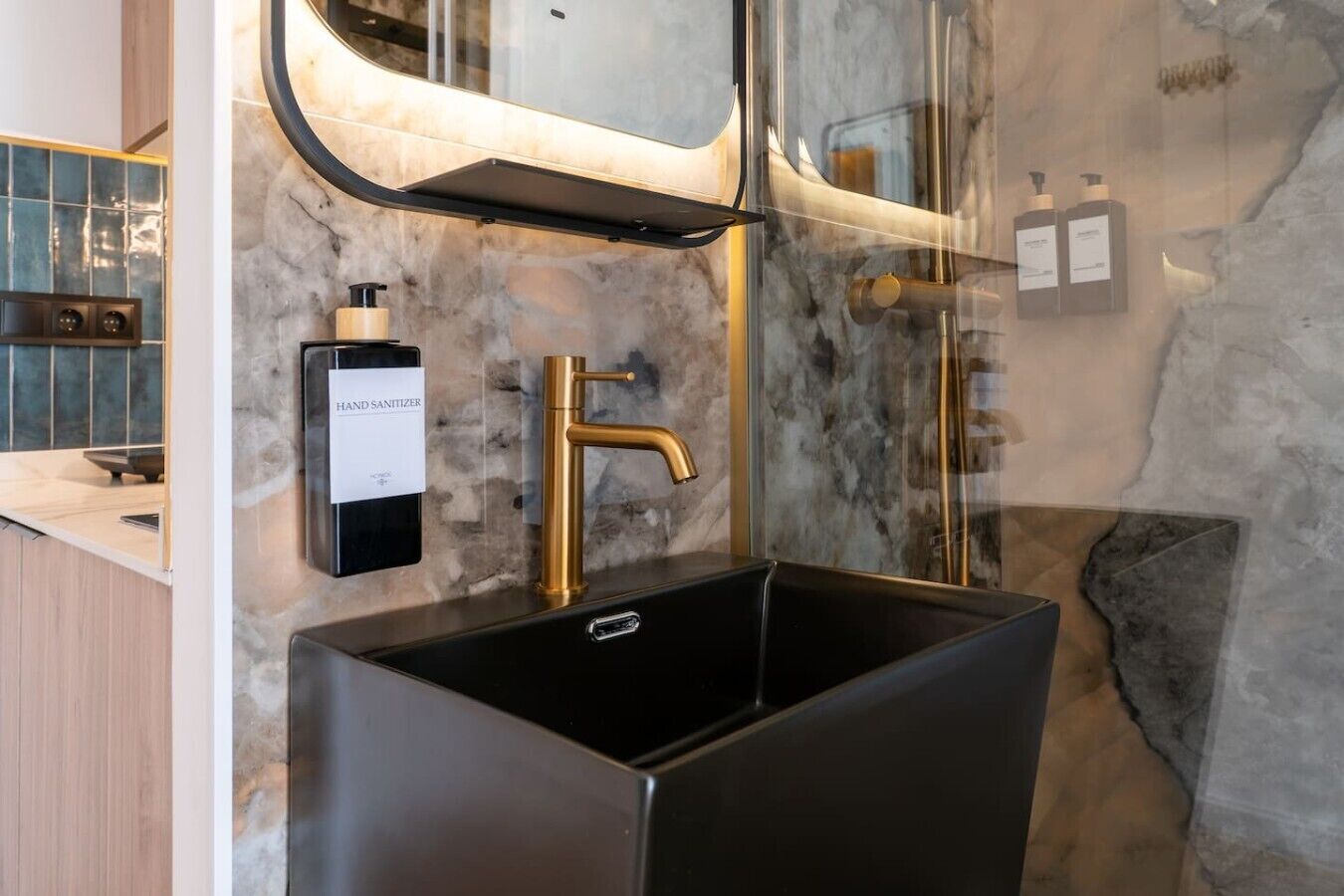 A modern bathroom with a large black sink, a gold faucet, and a hand sanitizer dispenser.