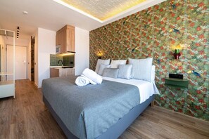 A modern bedroom with a large bed, a built-in kitchen, and a patterned wallpaper. - Sol Atelier | Apartments by Monaro* * * * * (Madrid)