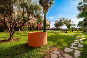 Un jardin agrémenté d’un grand pot en terre cuite, de chemins en pierre et de différents arbres.