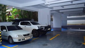 Un parking couvert où sont garées deux voitures, avec des emplacements de stationnement délimités et un sol bleu.