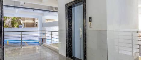 Un vestíbulo moderno y limpio con suelo de mármol, un diseño en forma de estrella, un ascensor de vidrio y una barandilla de metal.