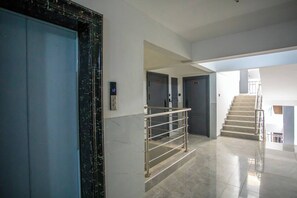 Un interior moderno con suelo de mármol, una escalera y un panel digital de ascensor.