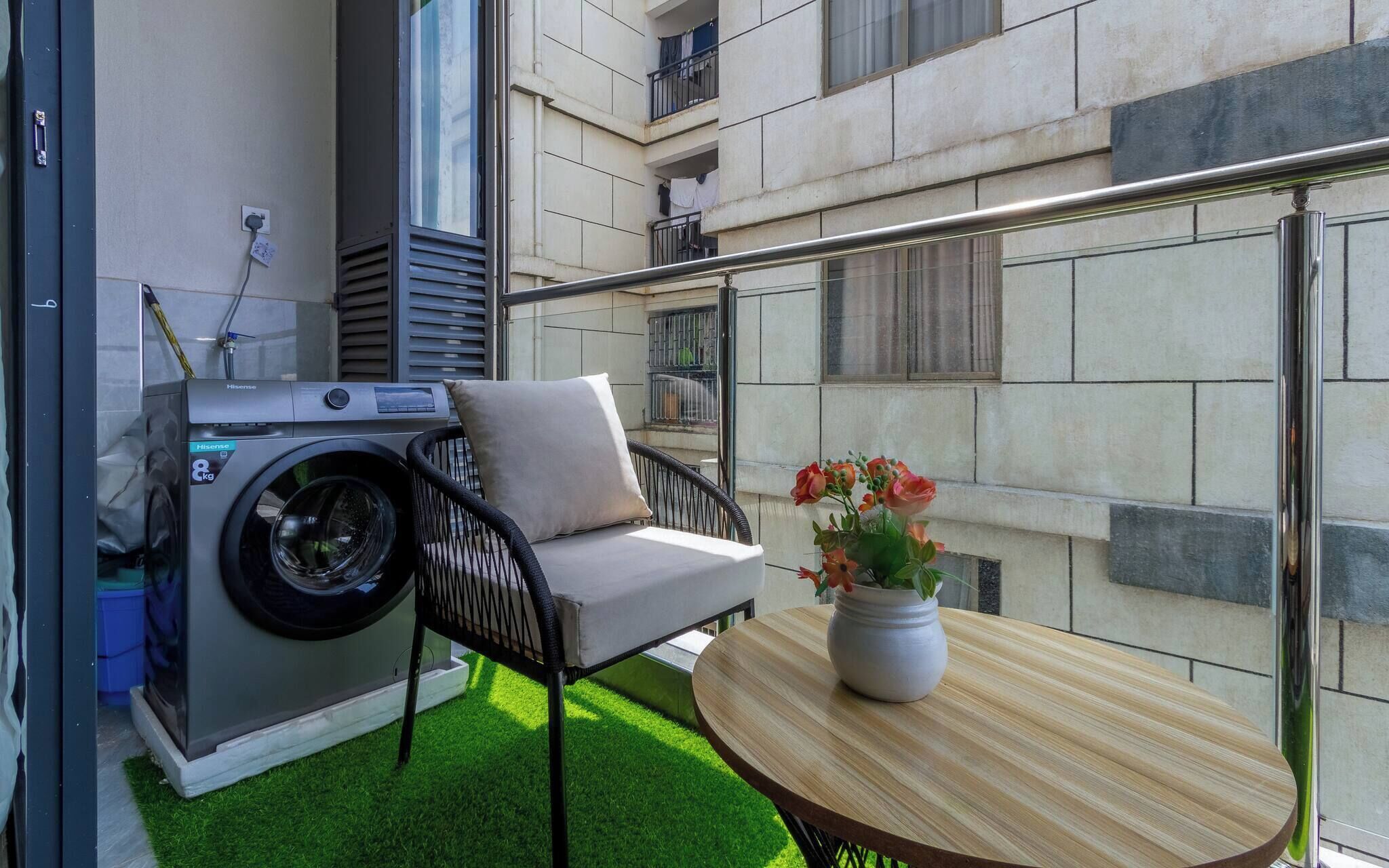 Un balcón con lavadora, una silla y una mesa con flores.