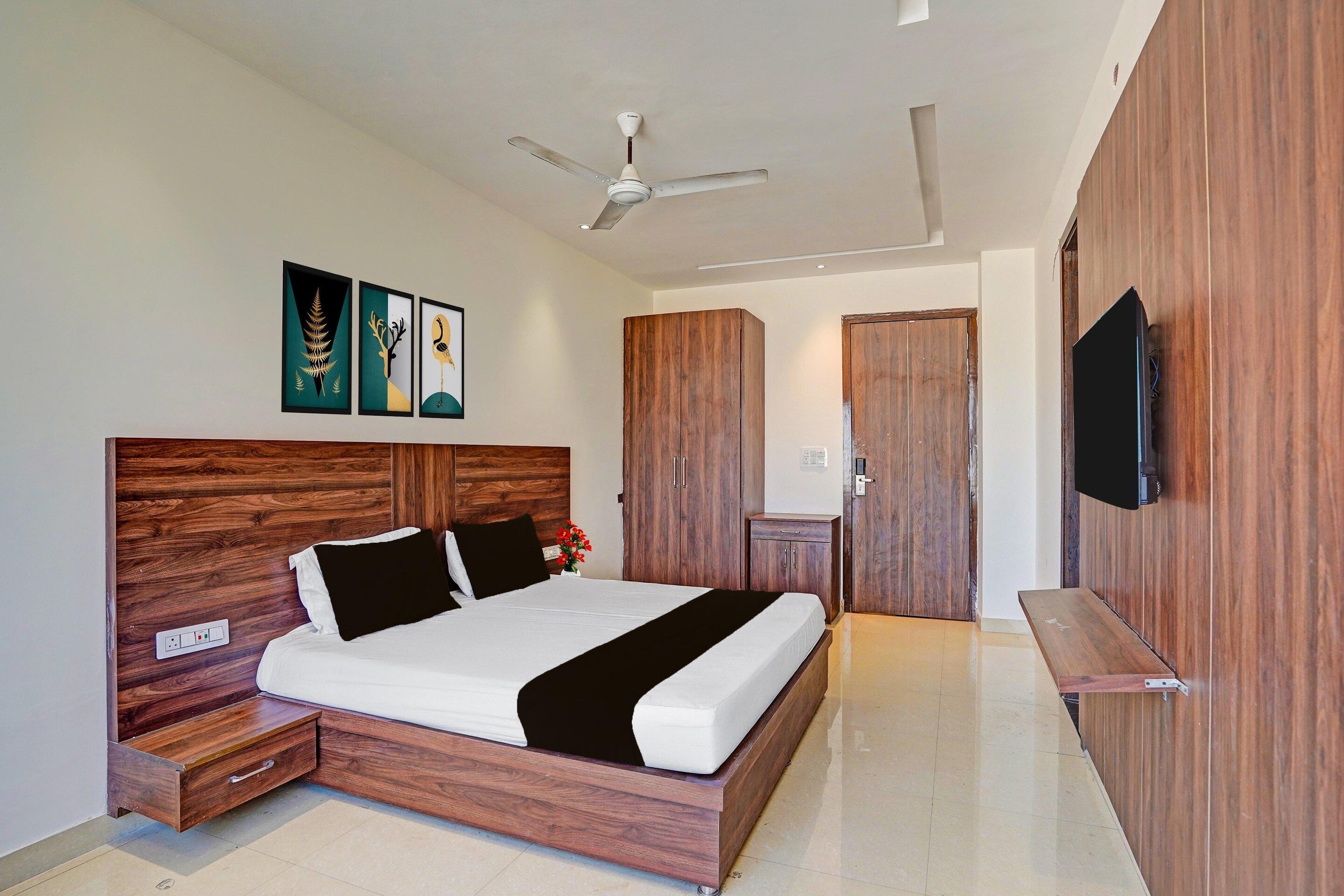 Ein Schlafzimmer mit einem Holz-Kopfteil, einem Bett mit weißer Bettwäsche, einem Nachttisch und einem Wandtelevisionsgerät sowie einem Deckenventilator.