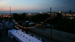 Terraza en la azotea con mesas preparadas para comer, con vista a un paisaje urbano al anochecer.