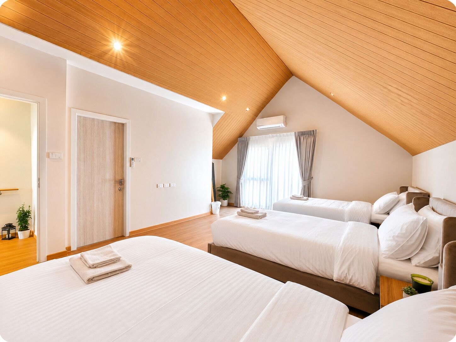 A hotel room with two beds, a wooden ceiling, and a large window with curtains.