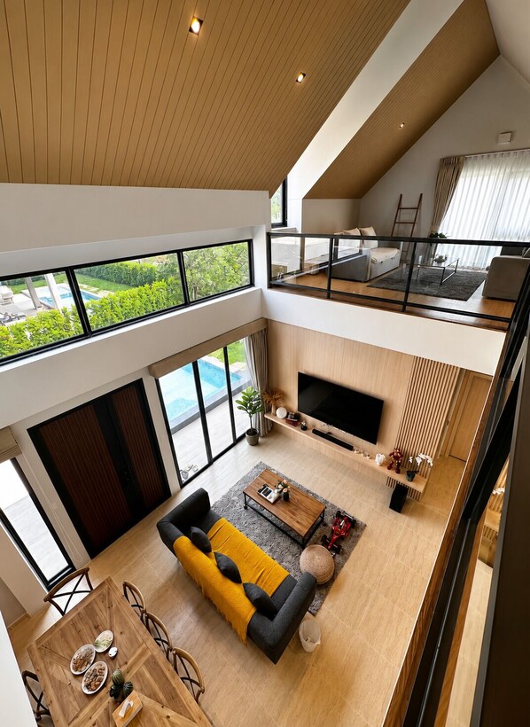 A modern multi-level living space with a dining area, a sofa, a TV, and a balcony overlooking greenery.