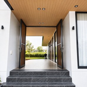 A modern building entrance with a wooden ceiling, large glass doors, and a tiled floor leading to a covered outdoor area.