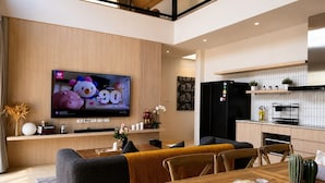 Una sala de estar moderna con un televisor de pantalla plana, un comedor con mesa de madera y una cocina con refrigerador negro.