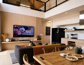 Una sala de estar moderna con un televisor de pantalla plana, un comedor con mesa de madera y una cocina con refrigerador negro.