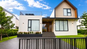 Una casa moderna de dos pisos con techo plano, ventanas grandes y un balcón pequeño.