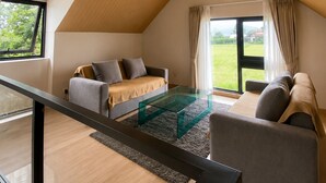 Un dormitorio estilo loft moderno con techo inclinado, una mesa de centro de vidrio, un sofá y vistas a un paisaje verde.