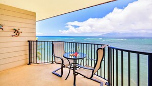 A balcony with a table and chairs, overlooking a view of the ocean and a distant mountain. - New Listing Oceanview Guaranteed (Lahaina)
