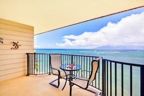 Ein Balkon mit Tisch und Stühlen, der Blick auf das Meer und ein entferntes Gebirge freigibt.