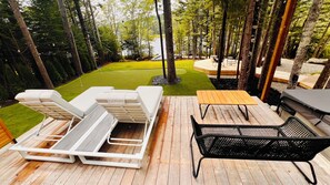 A deck with outdoor furniture, a grassy lawn, and a view of a lake. - The Lake Villa
Cedar Sauna, Hot Tub, and Private Putting Green 
Escape for Two (Ingramport)