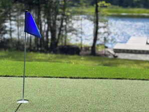 Golfkentän viheriöllä oleva golf-lippu, taustalla vesistö ja puita.