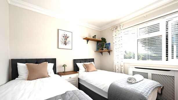 A hotel room with two beds, a window with blinds, a radiator, and a wall-mounted shelf with decorative items. - Milcourt -  a managed house that sleeps 8 guests  in 4 bedrooms (Canterbury)