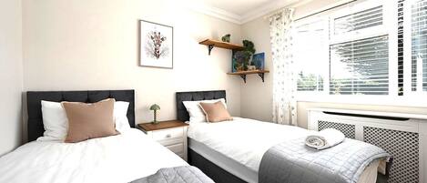 A hotel room with two beds, a window with blinds, a radiator, and a wall-mounted shelf with decorative items.