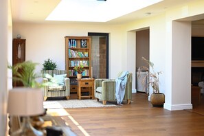 A cozy living room with a wooden bookshelf, striped armchairs, a small table, and a potted plant.