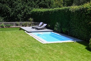 A rectangular swimming pool with a deck, surrounded by a well-maintained lawn and a wooden fence.