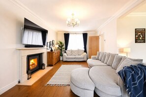 A living room with a fireplace, a sofa, a television, and a chandelier. - Milcourt -  a managed house that sleeps 8 guests  in 4 bedrooms (Canterbury)