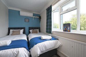A bedroom with two beds, a window with a view, a children's encyclopedia on the windowsill, and a wall-mounted air conditioner.