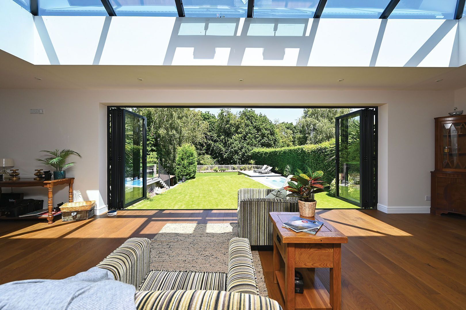 A modern living room with a large glass door leading to a well-maintained garden and pool.