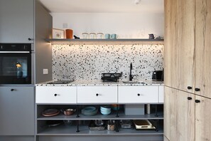 A modern kitchen with a speckled backsplash, white cabinetry, and a wooden cabinet door. - Pett Beach Landing -  a holiday let that sleeps 2 guests  in 1 bedroom (Hastings)