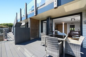 Une terrasse extérieure moderne, dotée de meubles en osier et d’une véranda en verre donnant sur un espace cuisine.