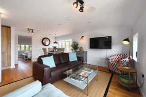 A modern living room with a brown leather sofa, a glass coffee table, and a colorful patterned chair. - Pett Beach Landing - a holiday let that sleeps 2 guests in 1 bedroom (Hastings)