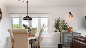 En matplats med ett runt bord, stolar, en hängande lampa, en krukväxt och ett grått skåp med lådor.