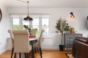 A dining area with a round table, chairs, a hanging light fixture, a potted plant, and a grey cabinet with drawers. - Pett Beach Landing -  a holiday let that sleeps 2 guests  in 1 bedroom (Hastings)