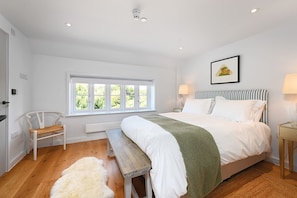 Une chambre à coucher avec un grand lit, un banc, une chaise, une fenêtre donnant sur un beau paysage et une lampe sur une table de chevet.