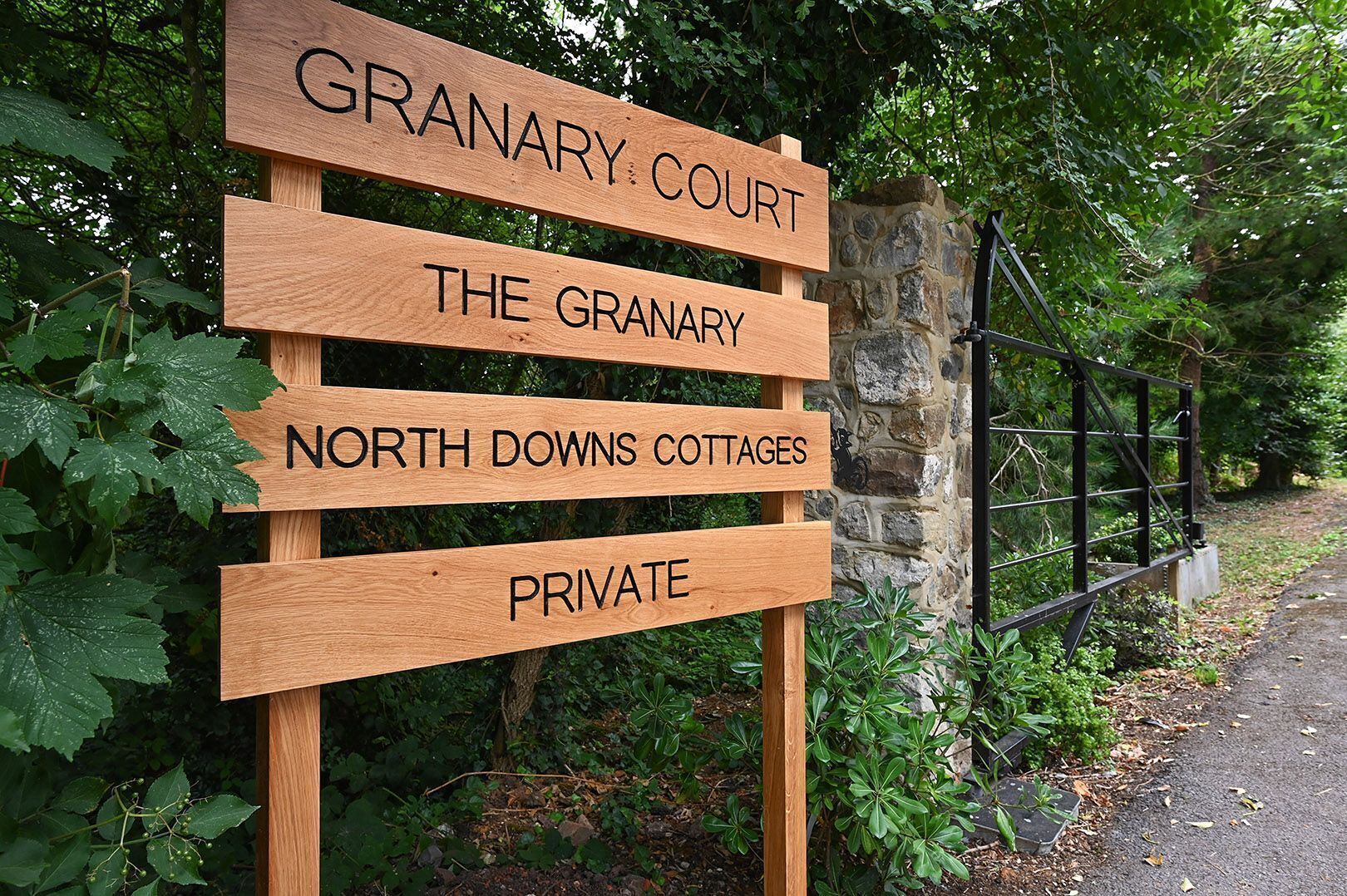 A wooden sign with text indicating 'GRANARY COURT,' 'THE GRANARY,' 'NORTH DOWNS COTTAGES,' and 'PRIVATE.'