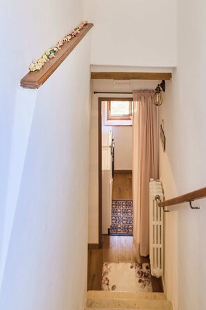 A staircase with a wooden handrail, a radiator, and a patterned rug in the background. - A romantic house with a garden in Val d'Orcia. Between the past and the present. (Monticchiello)