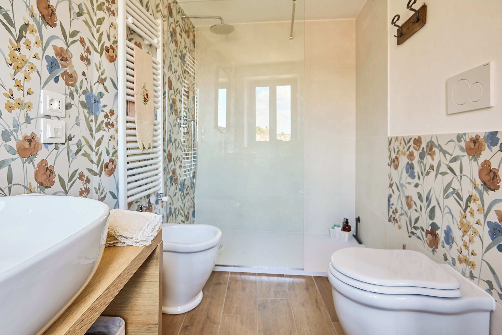 A bathroom with a shower, two toilets, a sink, and a wooden shelf.