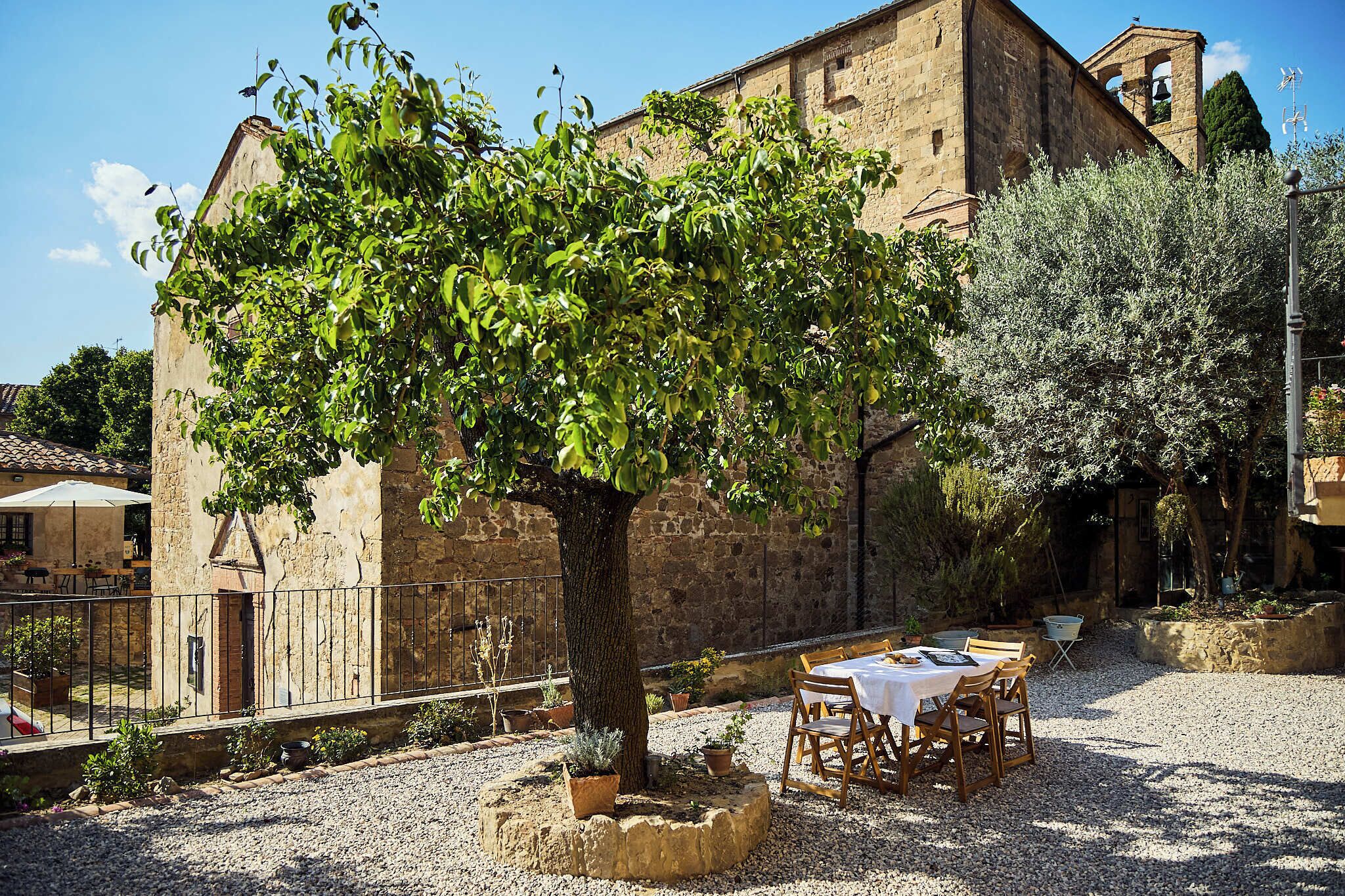 An outdoor seating area with a table and chairs, a tree, and a stone building with a bell tower.