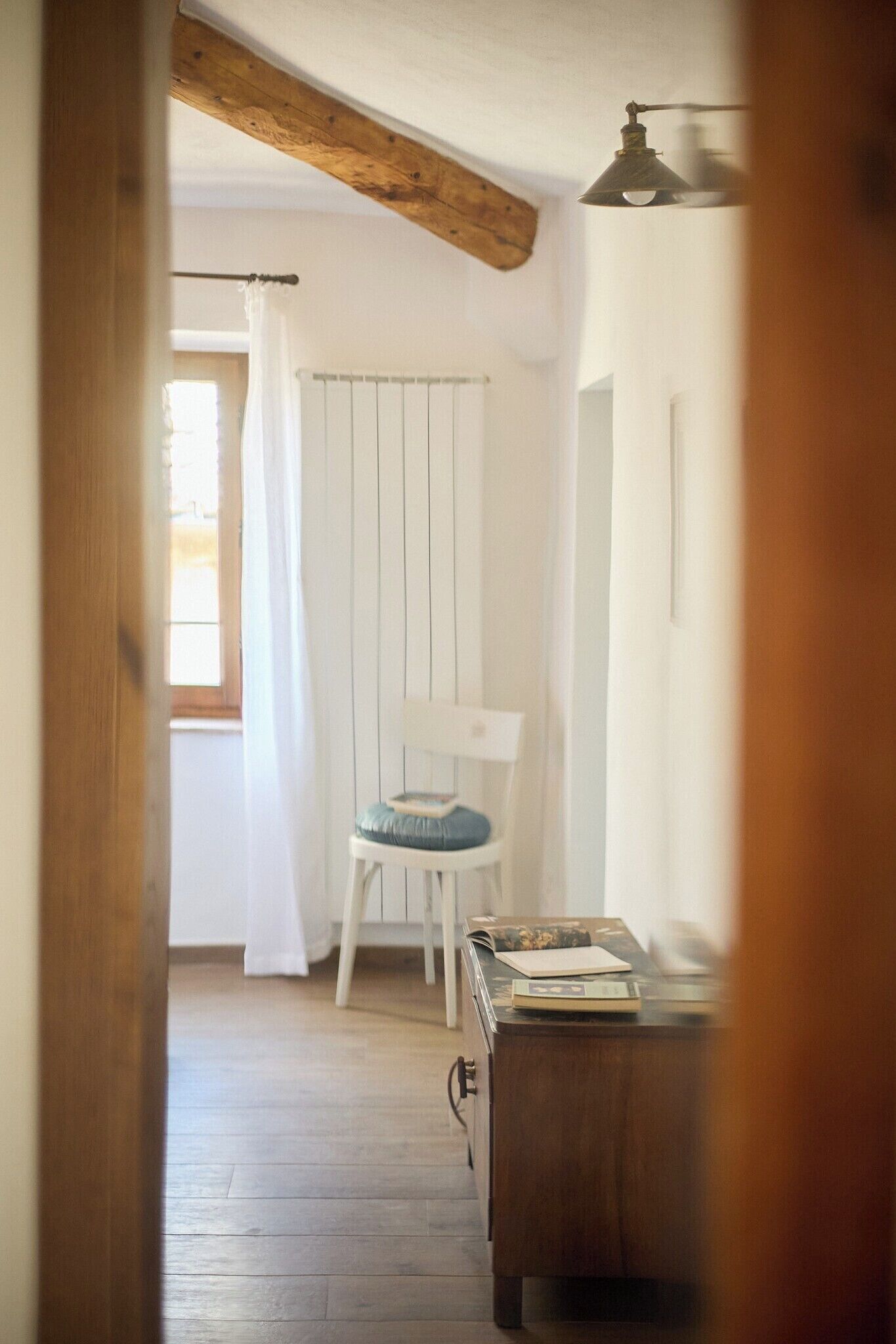 Ein Zimmer mit Holzboden, einem weißen Stuhl mit Kissen, einem kleinen Tisch mit einem Buch und einem Heizkörper.