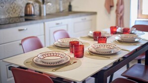 Ein Esstisch ist mit Tellern, Gläsern und Besteck in einer Küche mit einer gefliesten Spritzschutzwand und Schränken gedeckt.