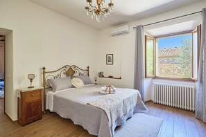 A bedroom with a bed, bedside table, lamp, radiator, and a window with a view. - A romantic house with a garden in Val d'Orcia. Between the past and the present. (Monticchiello)