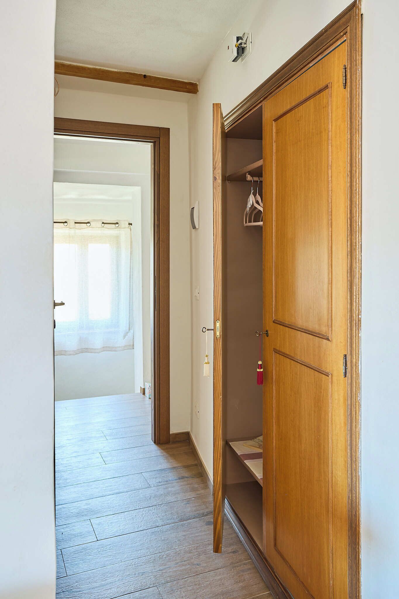 A hallway with a wooden wardrobe, a door leading to another room, and a window with curtains.