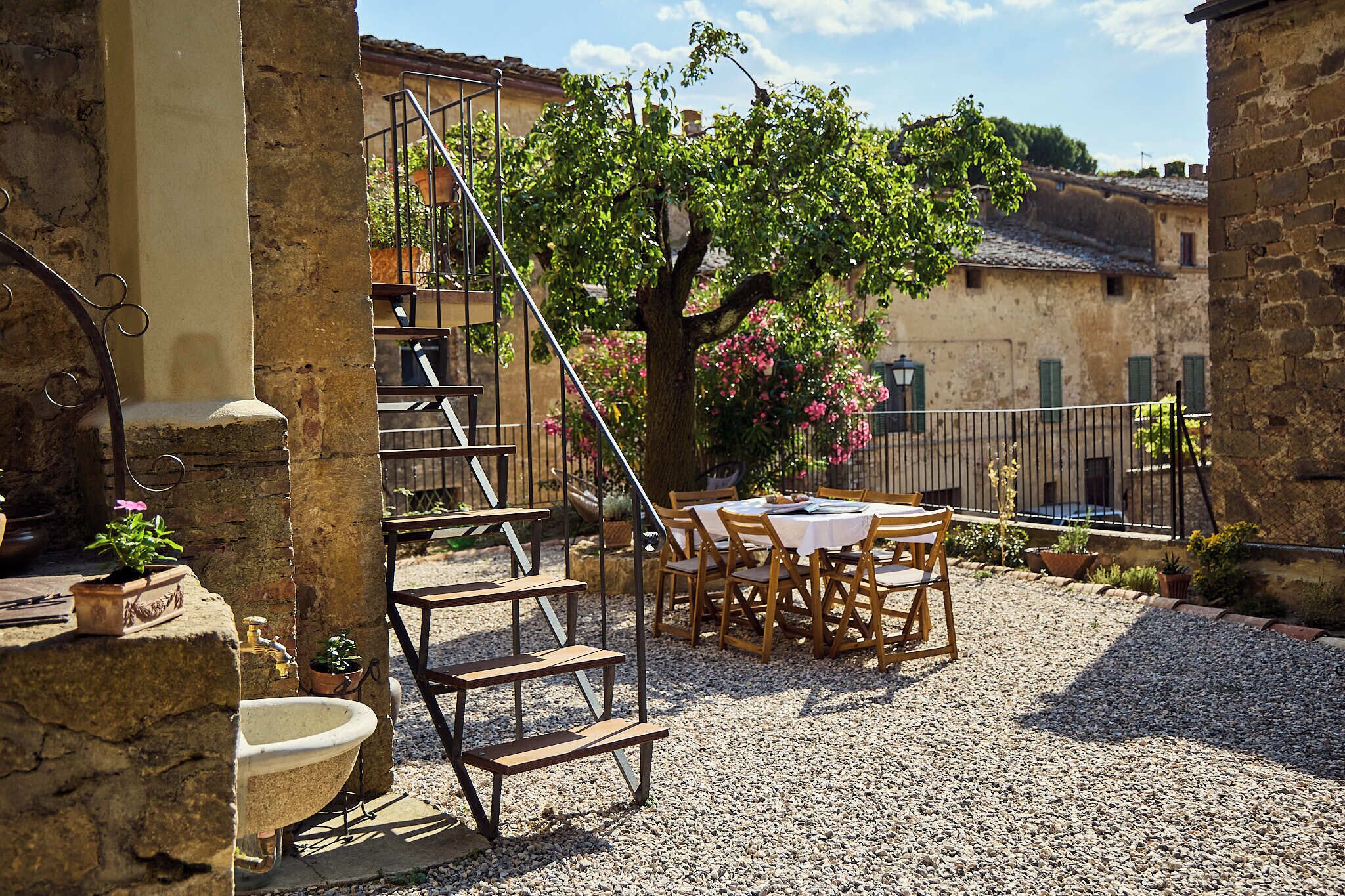 Un espace extérieur rustique aménagé avec un évier en pierre, des chaises en bois, une table et un escalier en métal.