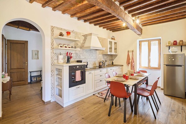 A kitchen with white cabinets, a stainless steel refrigerator, and a dining area with red chairs. - A romantic house with a garden in Val d'Orcia. Between the past and the present. (Monticchiello)