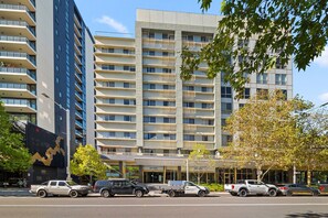 A multi-story hotel with a modern design, featuring a central entrance and a parking area with several vehicles. - Stylish 2-bed Stay With Pool & Parking (Canberra)