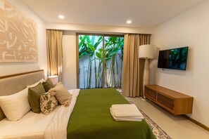 Ein modernes Schlafzimmer mit Bett, Fernseher, Lampe und Blick auf Grün durch eine Glastür.
