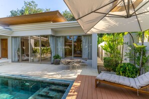 A modern outdoor pool area with a wooden deck, a lounge chair, and a covered seating area. - Private Pool Villa in the Heart of Bang Tao (ต.เทพกระษัตรีย์)