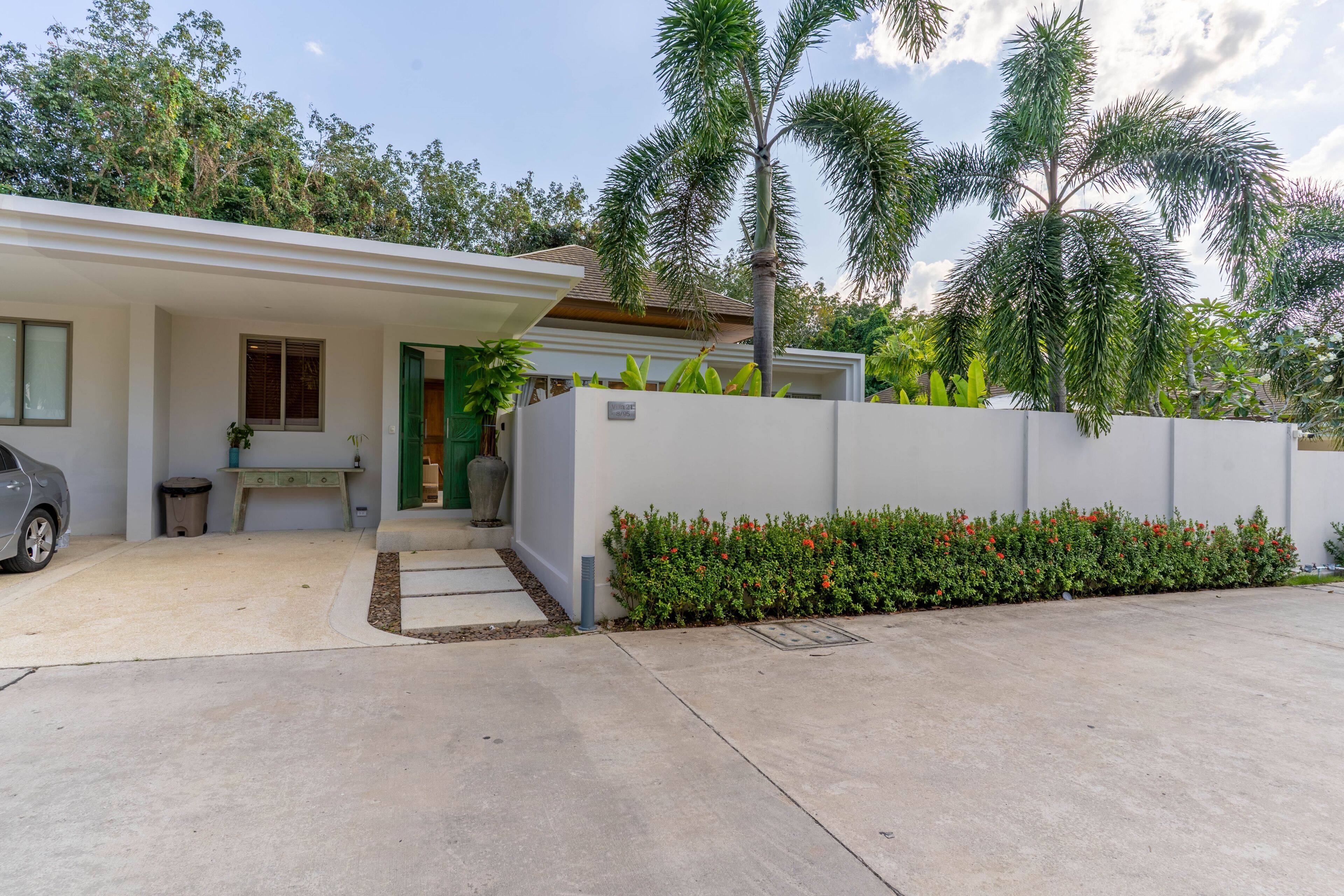 Una casa moderna con fachada blanca, garaje y un jardín bien cuidado con flores rojas.
