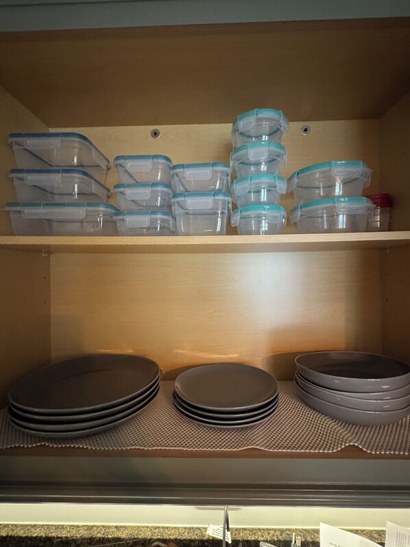 A storage shelf with clear plastic containers and a stack of plates.